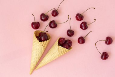 Waffle konilerinde taze kiraz. Dondurma konisi pembe bir arka plan üzerinde taze kiraz ile dolu. Üst te. Kopya alanı. Yaz konsepti.  
