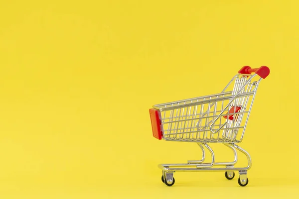 ショッピングカート 黄色の背景にショッピングトロリーのクローズアップ 買い物の概念 スペースのコピー — ストック写真