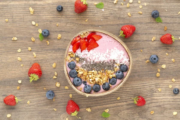 Smoothie bowl with granola, yogurt, Chia, strawberry and fresh blueberries on wooden background. Breakfast smoothie bowl, top view.