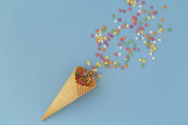 Mavi arka plan üzerinde renkli sprinkles ile dondurma konisi. Birden fazla renkli serpin nokta kalpleri. Kavramsal yaz geçmişi. Üst görünüm, kopyalama alanı. 