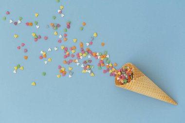 Mavi arka plan üzerinde renkli sprinkles ile dondurma konisi. Birden fazla renkli serpin nokta kalpleri. Kavramsal yaz geçmişi. Üst görünüm, kopyalama alanı. 