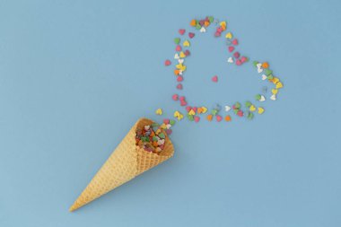 Mavi arka plan üzerinde renkli sprinkles ile dondurma konisi. Birden fazla renkli serpin nokta kalpleri. Kavramsal yaz geçmişi. Üst görünüm, kopyalama alanı. 