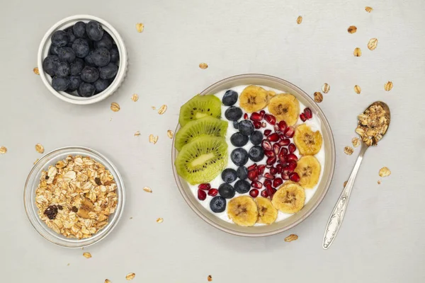 Breakfast smoothie bowl. Smoothie bowl with fresh kiwi, blueberry, pomegranate, granola, banana and yogurt. Grey background.
