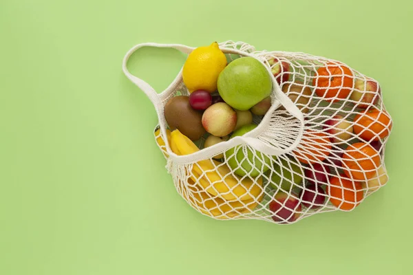 Yeşil arka plan üzerinde organik meyve ile çevre dostu örgü çanta. Sağlıklı temiz beslenme diyet ve detoks. Yaz meyveleri. Çevreye önem verme ve plastik kavramın reddi.