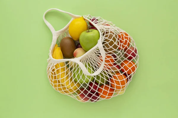 Yeşil arka plan üzerinde organik meyve ile çevre dostu örgü çanta. Sağlıklı temiz beslenme diyet ve detoks. Yaz meyveleri. Çevreye önem verme ve plastik kavramın reddi.