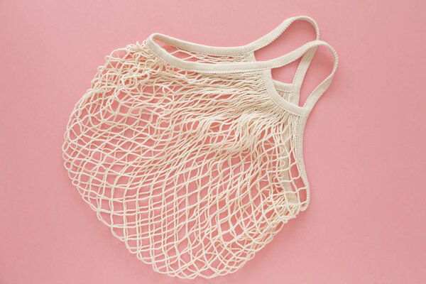Eco friendly mesh bag on pink background. Concept caring for the environment and the rejection of plastic. Reusable net bag or mesh shopper. Flat lay. Top view. 