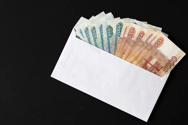 Siyah arka planda ruble banknotlu zarf. Rüşvet. Beyaz zarftan çıkan büyük ruble banknotlarını istifleyin. Kavram nakit rüşvet ve yasadışı sus para yolsuzluk.  
