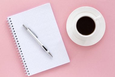 Pembe arka planlı okul defteri. Boş not defteri beyaz sayfa, kalem ve kahve, renkli arka plan. Üst görünüm, metin için alan.   