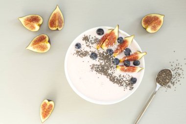 Sağlıklı kahvaltı berry smoothie kase incir, hindistan cevizi ve chia tohumları ile tepesinde. Taze olgun yaban mersini, incir, yoğurt, hindistan cevizi ve chia ile bir smoothie kase üst görünümü. Sağlıklı beslenme ve yaşam tarzı kavramı. 