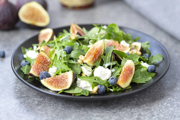 Keçi peynirli incir salatası, yaban mersini, çam fıstığı ve gri arka planda arugula ile. Vejetaryen yemekler.