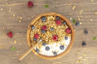 Ahşap arka plan üzerinde granola ve çilek taze ahududu ve yaban mersini ile Yoğurt. Üst te. Lezzetli ve sağlıklı Kahvaltı smoothie. Vejetaryen yemekler.