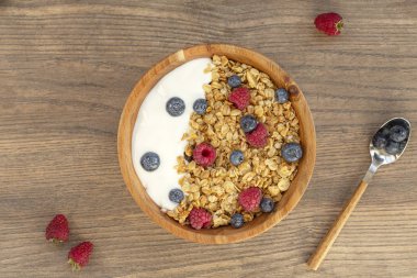 Ahşap arka plan üzerinde granola ve çilek taze ahududu ve yaban mersini ile Yoğurt. Üst te. Lezzetli ve sağlıklı Kahvaltı smoothie. Vejetaryen yemekler.