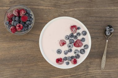 Ahşap arka plan üzerinde dondurulmuş ahududu, yaban mersini ve hindistan cevizi talaş ile Yoğurt smoothie. Sağlıklı gıda kavramı. Üstte görüntü.