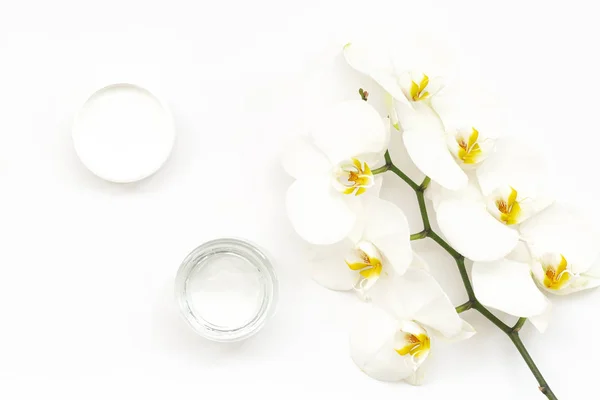 Beyaz arka plan üzerinde nemlendirici yüz jeli ve güzel orkide çiçekleri. Güzellik Spa konsepti. Jel ve Beyaz Phalaenopsis orkide ile açılan plastik konteyner. Organik Doğal kozmetik.