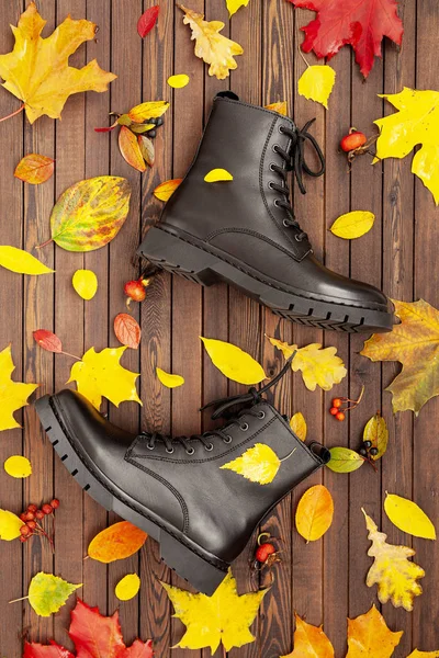 Women's autumn shoes. Fashionable casual boots for walks, on a dark wooden background with autumn leaves. Flat lay. Autumn Fashion Concept.