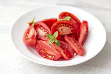 Fesleğen ve zeytinyağlı domates salatası, beyaz ahşap arka plan. Sağlıklı yemek kavramı. Vejetaryen yemeği. 