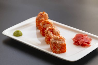 Japon deniz ürünleri suşisi. Suşi ruloları, wasabi, turşulu zencefil ve çubuklar beyaz tabakta.