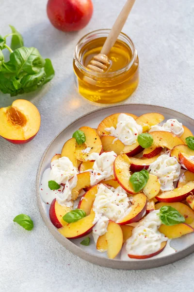 Şeftalili taze salata, İtalyan Stracciatella peyniri, fesleğen, zeytinyağı ve bal. Yaz salatası, sağlıklı gıda konsepti. Seçici odak