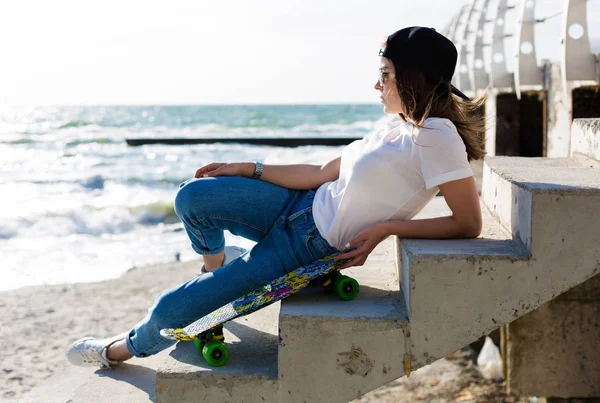Beautiful yound woman with a skateboard on a beach