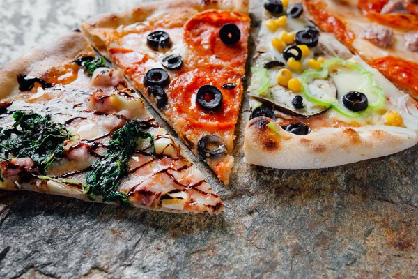 Compound pizza from slices of different pizzas ,  black background on  stone with flour, sliced peppers,  Top view. Banner, close-up, copy-space