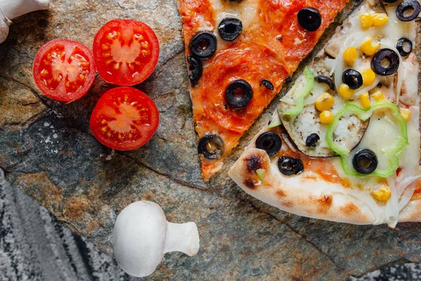 Compound pizza from slices of different pizza,  decorated with sliced tomatoes and mushrooms, sliced peppers,  black background on  stone with flour, Top view. Banner, close-up, copy-space