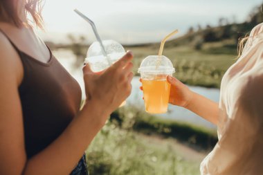 yakın kapatın. portakal suyu ile iki plastik bardak ile kızlar, saman ile, gün batımında, açık