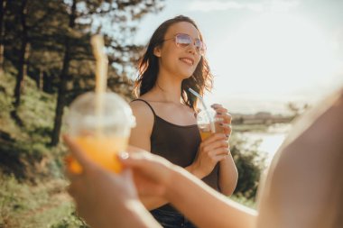 iki güzel kız arkadaş, yaz aylarında eğlenmek, güneş gözlüğü suyu içme, beyaz ve siyah gömlek, doğada, gün batımında, pozitif yüz ifadesi, açık