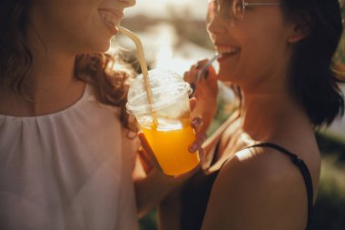 yakın kapatın. İki güzel kız gün batımında saman ile kokteyl içmek, olumlu yüz ifadesi, açık