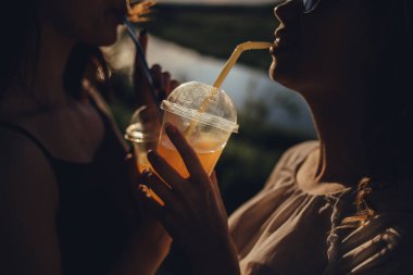 kapatın. İki güzel kız kız hipster kızlar sarılıyor ve birlikte eğlenmek, günbatımı bir kokteyl tutan, pozitif yüz ifadesi, açık