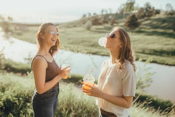 Duas Meninas Infla Uma Pastilha Elástica Beber Suco Copo Plástico — Fotografia de Stock