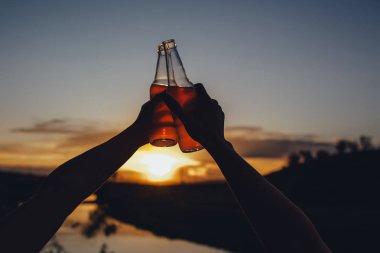 yakın kapatın. İki el, iki pembe şişe. kokteyl, meyve suyu, gün batımında, açık havada