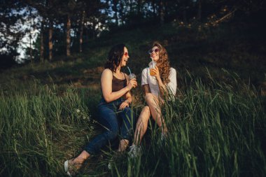 duygusal kız neşeli olsun, çim oturup, beyaz ve siyah gömlek güneş gözlüğü kokteyl içmek, gün batımında, olumlu yüz ifadesi, açık