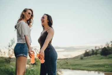 sevinç kavramı: iki meyve suyu şişesi ile iki kız, Kızlar gün batımında gün batımında kokteyller ile eğlenin, pozitif yüz ifadesi, açık