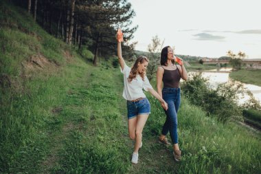 tatil ve mutluluk kavramı, iki kız eğlenmek, şişeden kokteyl içmek, yaz eğlencesi, gün batımında, pozitif yüz ifadesi, açık
