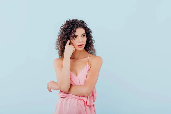 young and fashionable lady with curly hair dressed in a pink shirt, isolated on blue background, copy space