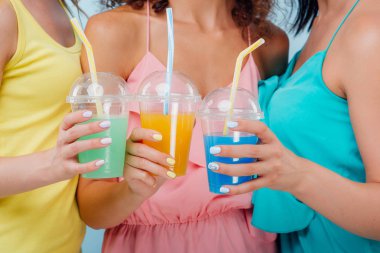 farklı meyve suyu renkleri ile üç plastik bardak, üç el, izole mavi kopya alanı