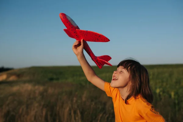 Sincere emotions. Happy little girl running on the field with red toy plane in their hands, outdoors, sky background