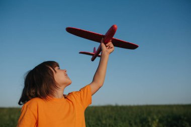 küçük kız kırmızı bir gömlek giymiş, kırmızı bir uçak tutar, uçan hayalleri, açık havada, gökyüzü arka plan