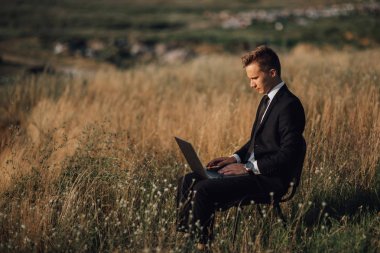 alanında dizüstü bilgisayar üzerinde çalışan genç işadamı, takım elbiseli sandalyede oturan, açık