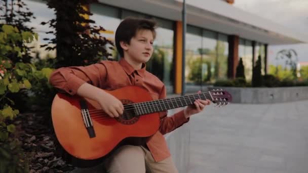 男孩弹吉他，坐在路边，穿着衬衫, — 图库视频影像