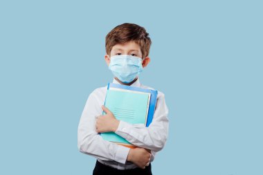 Tıp maskeli okul çocuğu, elinde defterler ve kitaplar var.