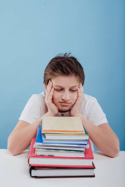 Masada oturan, kitapları olan yorgun çocuk.,