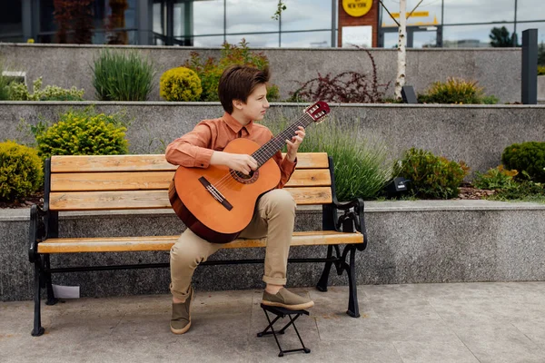 Bel enfant avec guitare assis sur une chaise dans le parc, vêtu d'une chemise , — Photo