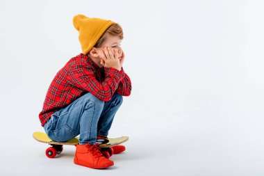 Yorgun küçük çocuk kaykayın üzerinde oturuyor.,