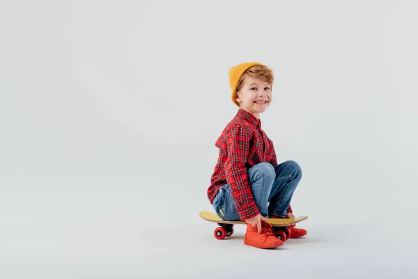 Маленький и счастливый мальчик смотрит в камеру, сидит на скейтборде — стоковое фото