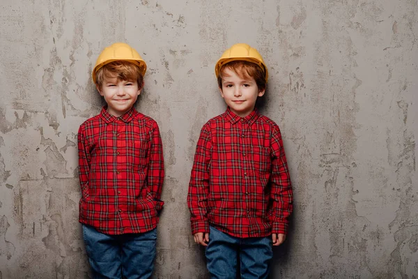 Два усміхнених маленького хлопчика з будівельників шолом, дивлячись на камеру , — стокове фото