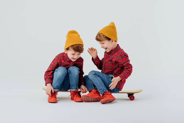 Blij tweelingbroers zitten op skateboards en lachen — Stockfoto