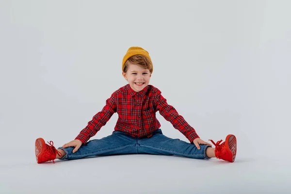 Cheerful boy in checkered shirt on floor in studio — Stock Photo, Image