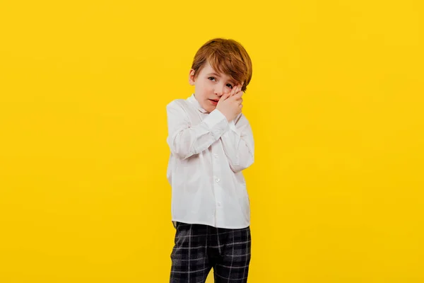 Грустный маленький мальчик с рукой на лице, одетый в белую рубашку — стоковое фото
