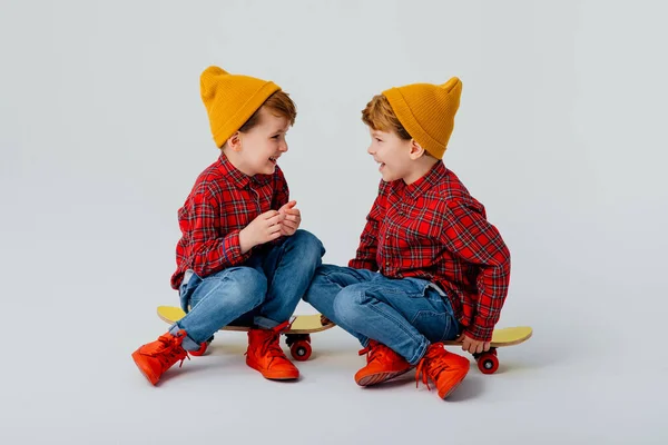 Два усміхнених маленьких хлопчика сидять на скейтборді — стокове фото